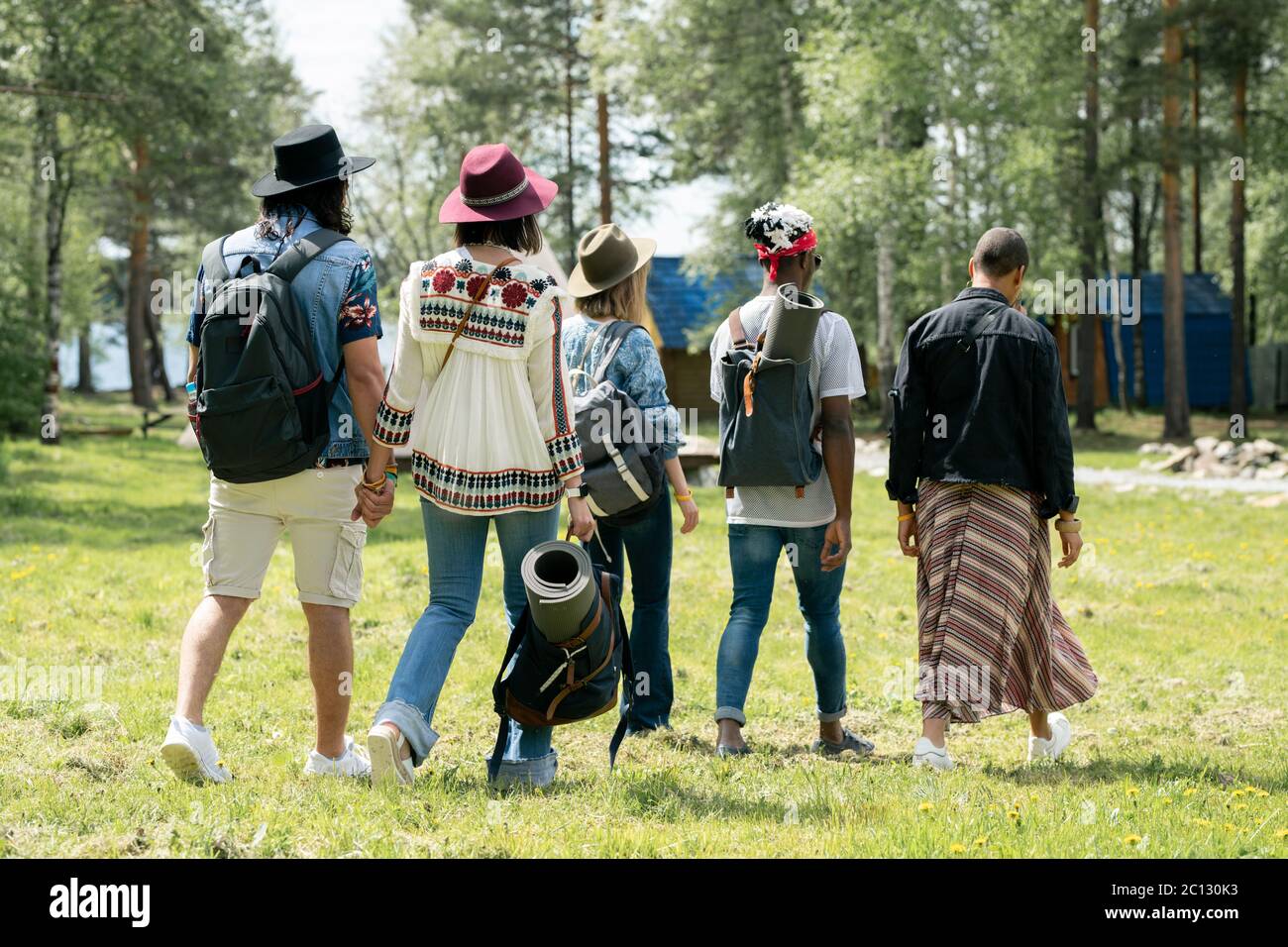 Vista posteriore di giovani amici multietnici con scacchi a piedi sul campeggio festival, mentre trovare posto per il campeggio Foto Stock