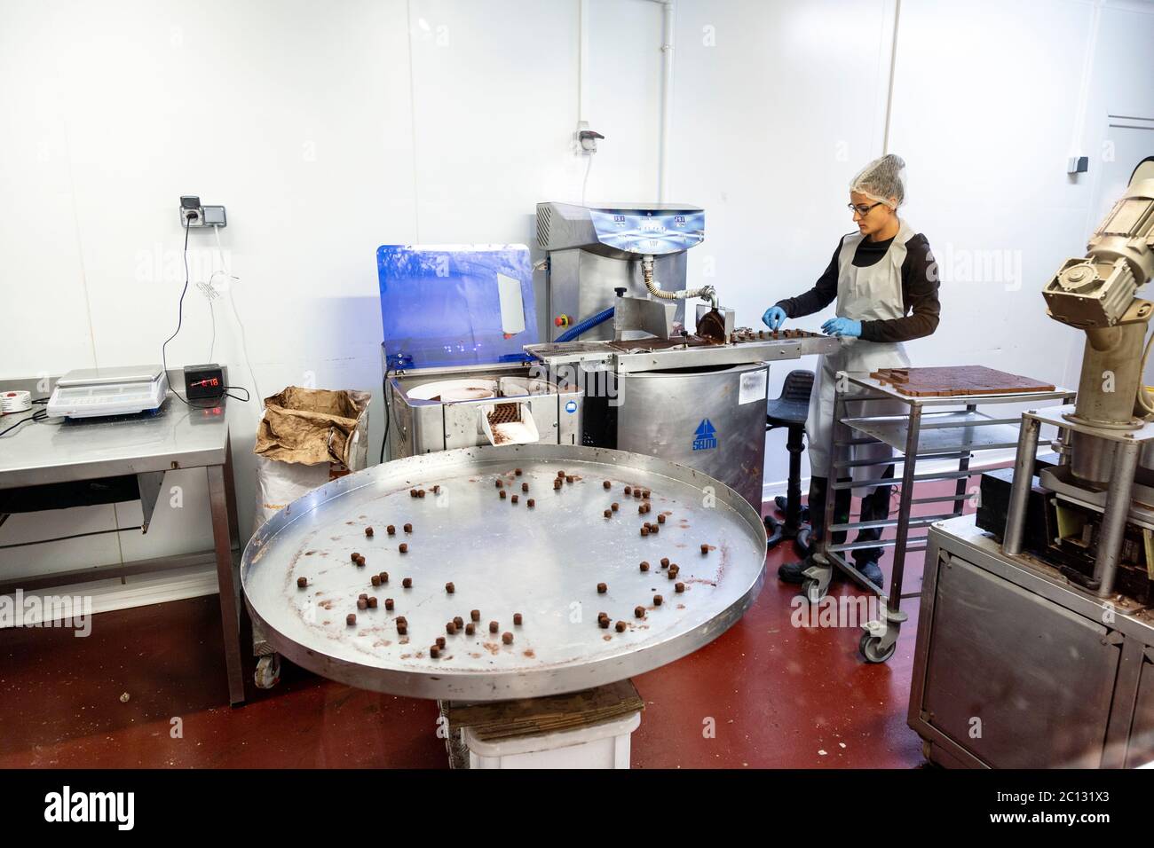 Lavoratore di fabbrica di cioccolato che mette le praline sul nastro trasportatore da rivestire, l'Atelier du Chocolat, Musée du Chocolat, Museo del cioccolato, Bayonne, Francia Foto Stock