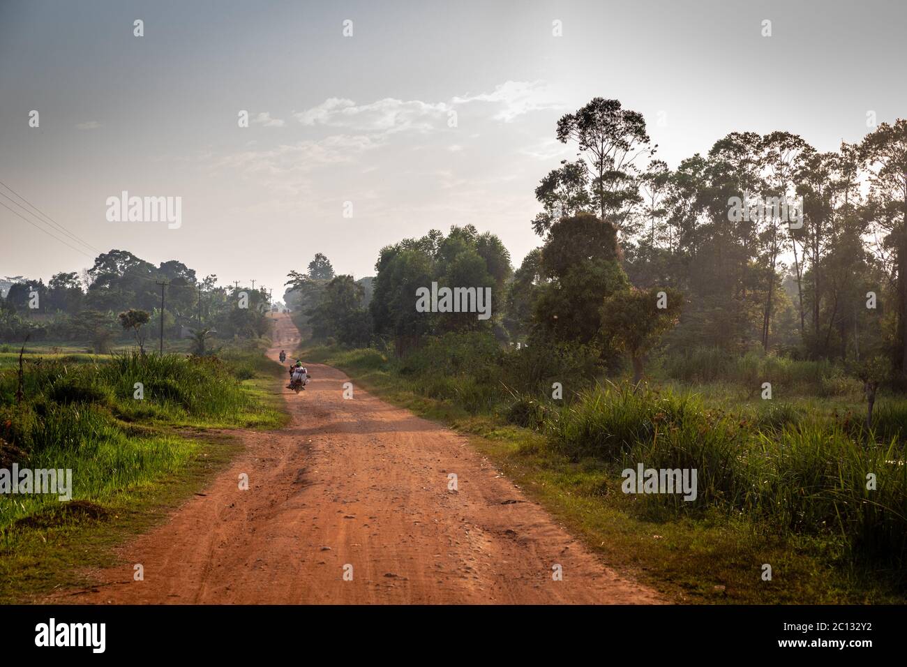 Una moto che viaggia lungo una strada sterrata non sigillata arancione vicino a Jinja, Uganda, Africa Foto Stock