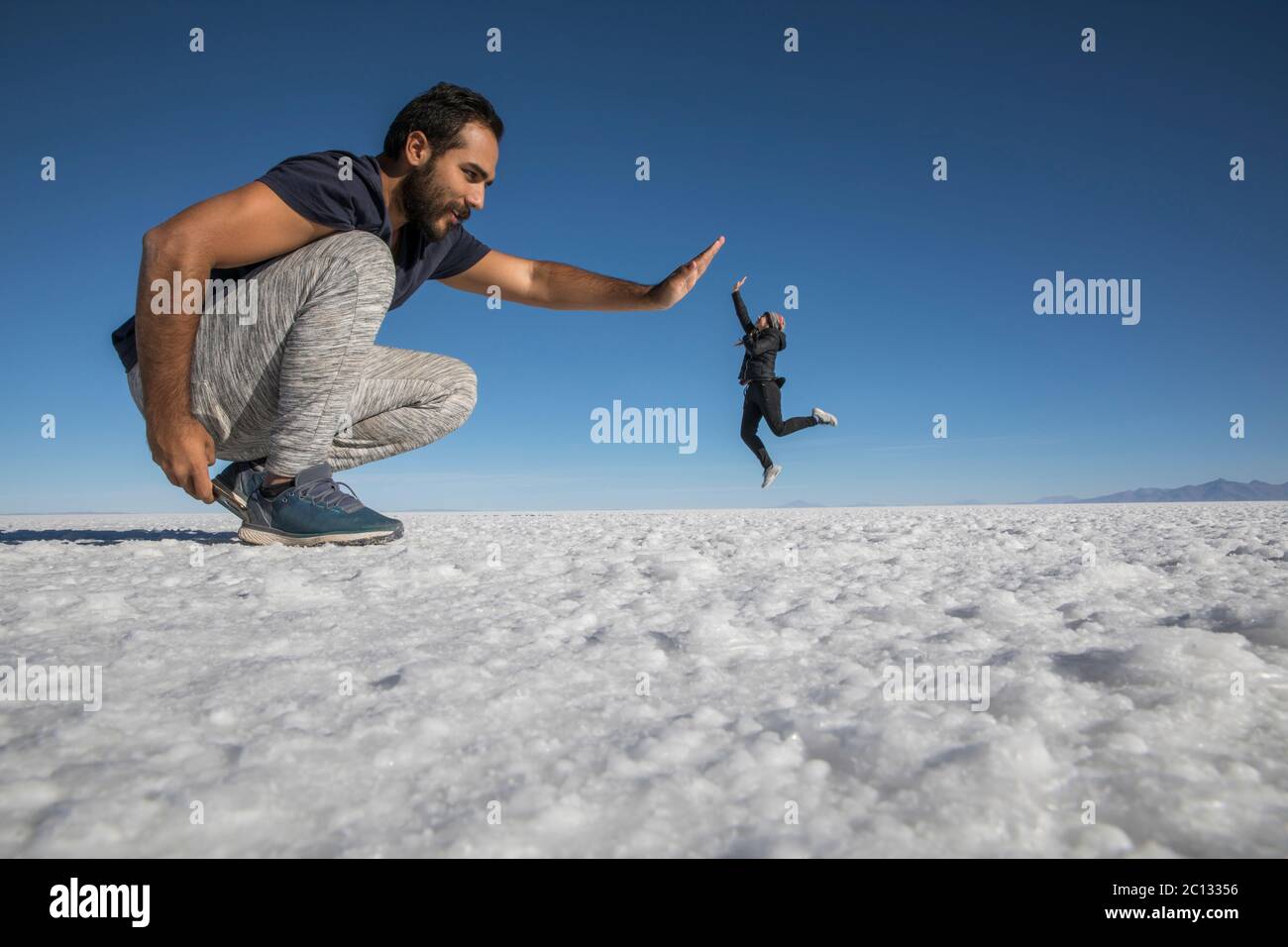 Coppia che gioca nelle saline del deserto, divertendosi con la prospettiva Foto Stock