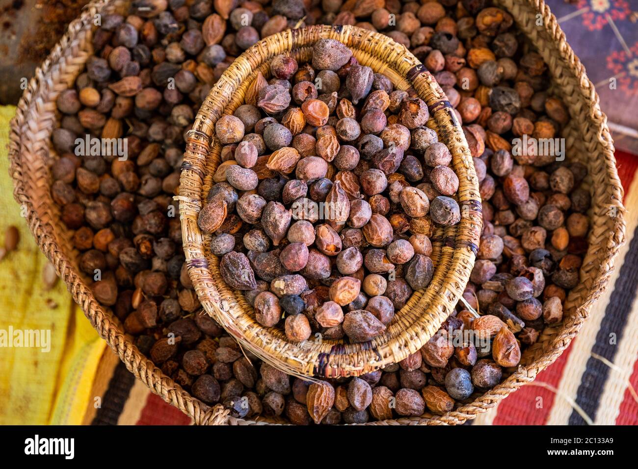 Close up di Argan dadi (Argania spinosa) in una cooperativa cesto di paglia in Marocco. Prodotti in Marocco, questo frutto è usato in cucina e prodotti cosmetici. Foto Stock