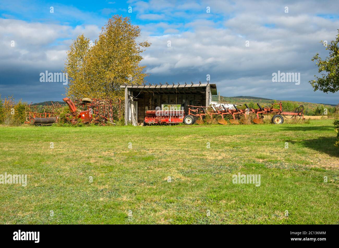 Attrezzature agricole e un vecchio capannone di legno in un campo con nubi tempesta incombente Foto Stock