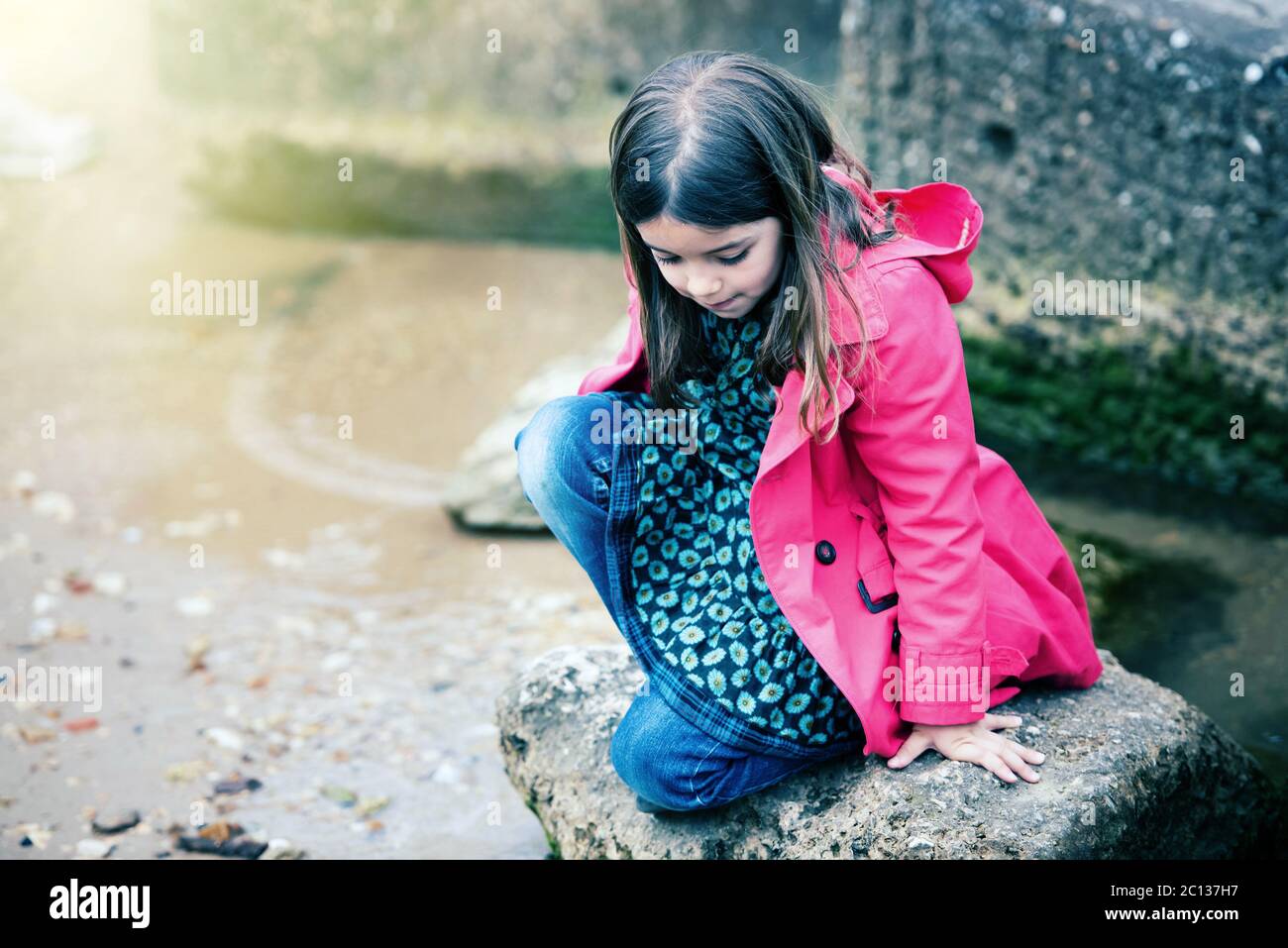 bella bambina che gioca su una roccia al bordo dell'acqua Foto Stock