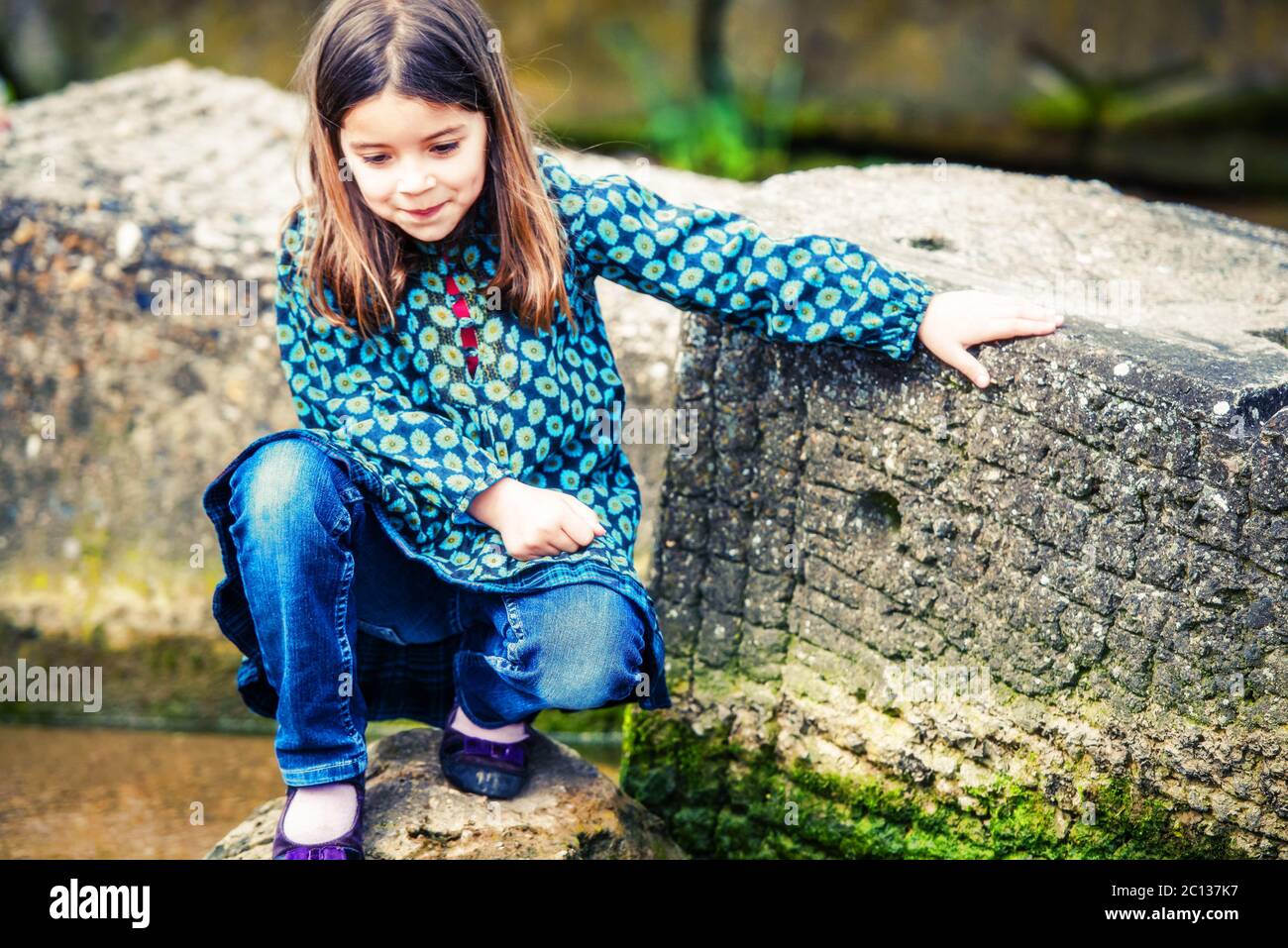 bella bambina che gioca su una roccia al bordo dell'acqua Foto Stock