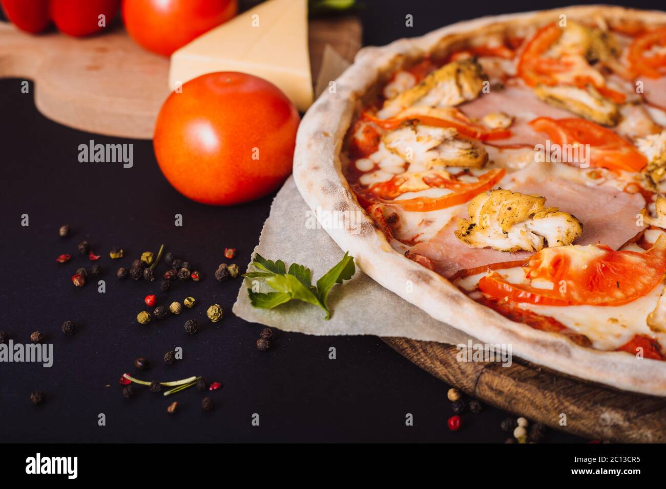 Gustosa pizza italiana e ingredienti per cucinare pomodori, erbe, formaggio su fondo nero di cemento. Pizza con pancetta calda. Foto Stock