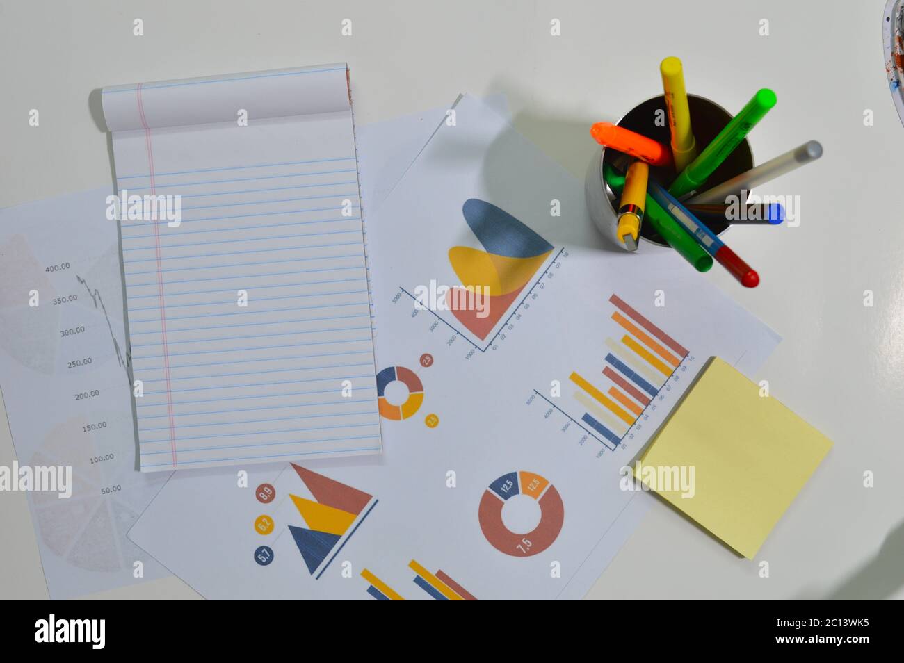 blocco note, grafico e penne su un tavolo che indica un'area di lavoro o un piano di lavoro Foto Stock