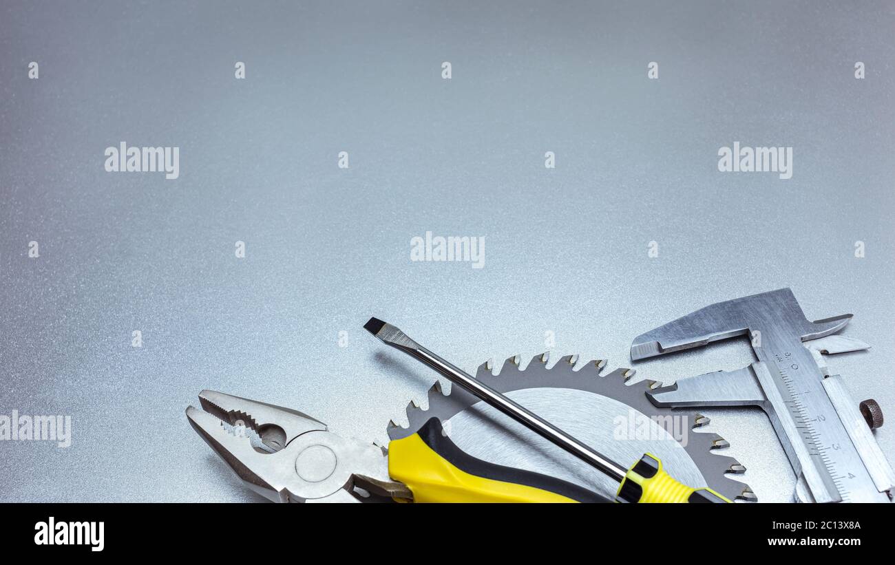 utensili manuali su fondo grigio in metallo - pinze, cacciavite, calibro a corsoio e lama per sega circolare Foto Stock