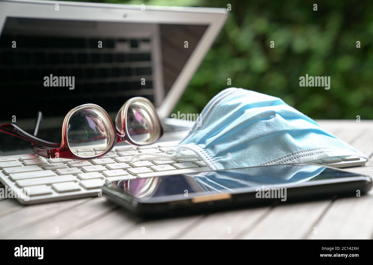 Maschera medica sulla tastiera del computer portatile con cellulare e occhiali sul tavolo. Lavorare a casa durante il concetto di covid-19. Foto Stock
