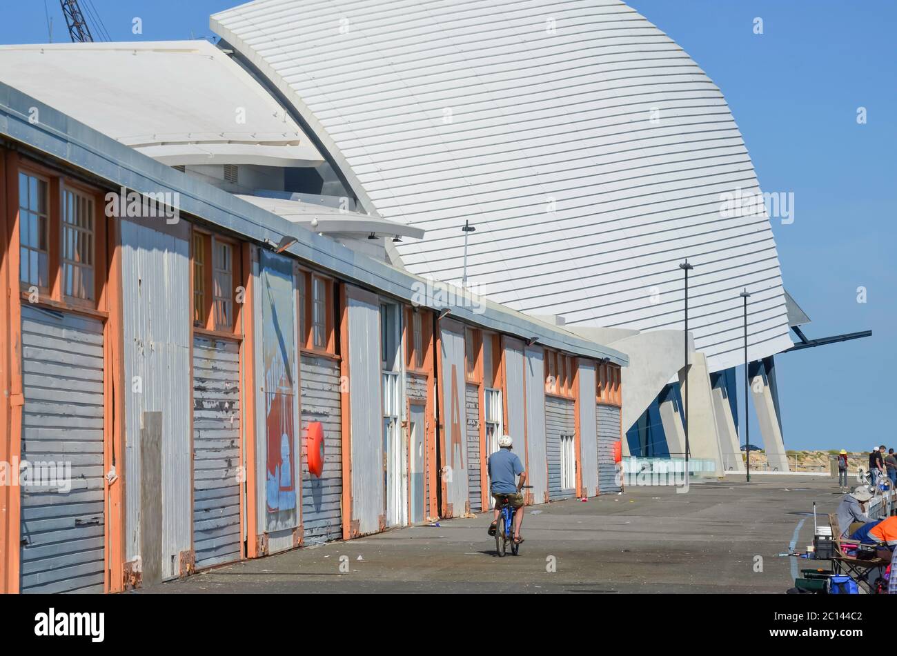 La gente pesca e un uomo cavalcano la sua bicicletta lungo il molo accanto al molo di Fremantle's A Shed vicino al museo marittimo WA nell'Australia occidentale Foto Stock