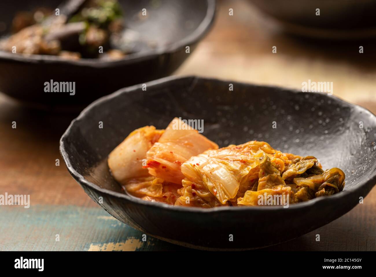 cavolo fermentato asiatico kimchi su una ciotola nera e altri ingredienti sullo sfondo Foto Stock