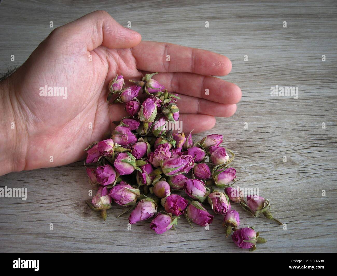 Boccioli di rosa secchi organici in mano maschile su sfondo di legno.  Concetto di aromaterapia. Boccioli di rosa essiccati per cosmetici, cibo,  medicina e profumo. Chiudi Foto stock - Alamy