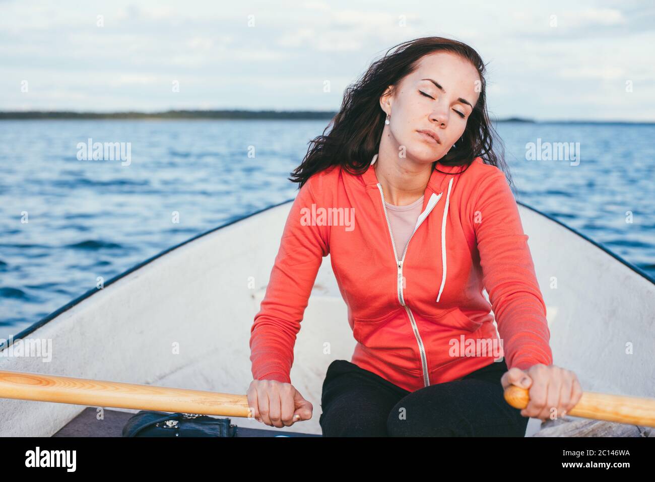 Incredibile bella ragazza dai capelli nuota su una barca di legno e canottaggio con remi in uno splendido lago di primavera. Stile di vita senza trucco Foto Stock