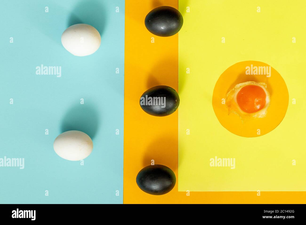 Due uova bianche con tre uova nere e un uovo schiacciato su un giallo con fondo blu. Foto Stock