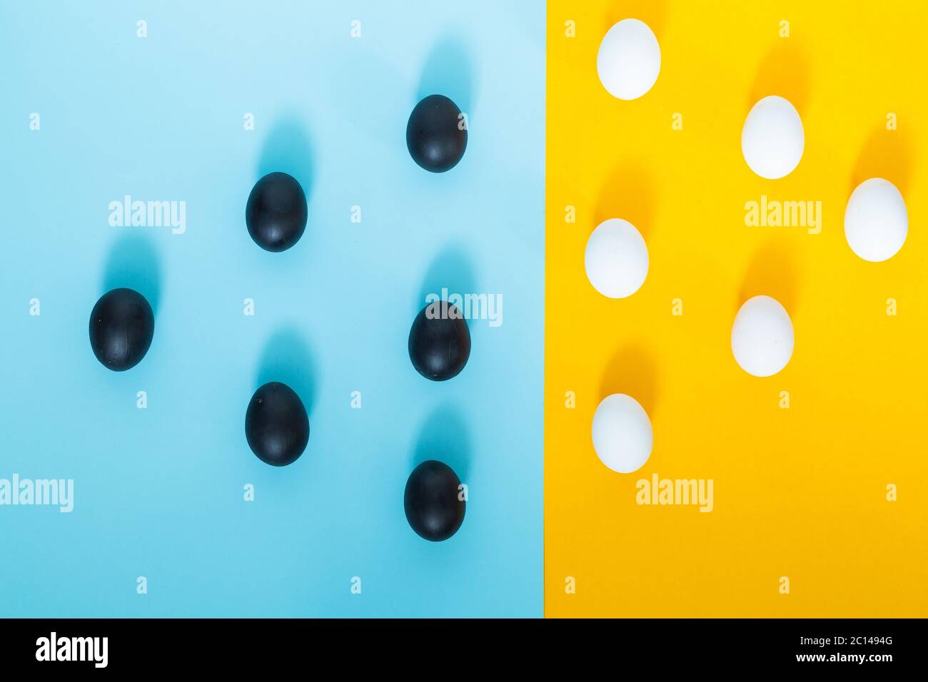 Uova nere e uova bianche su sfondo blu con giallo, astratto, decorativo, comparativo Foto Stock