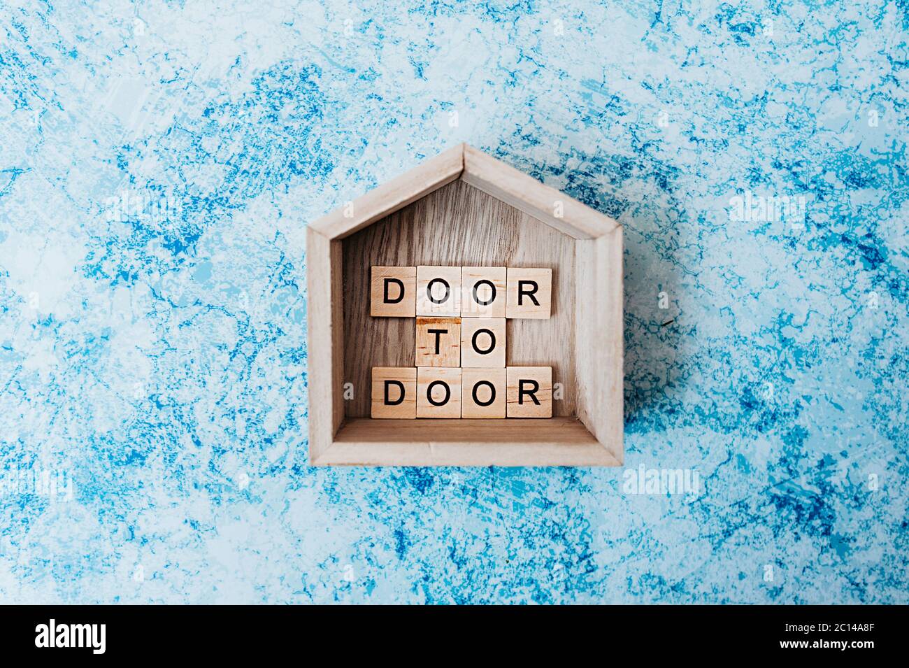 iscrizione porta a porta di lettere in legno in legno decorazione piccola casa con su un fondo grigio-blu cemento. consegna senza contatto e distanci sociali Foto Stock
