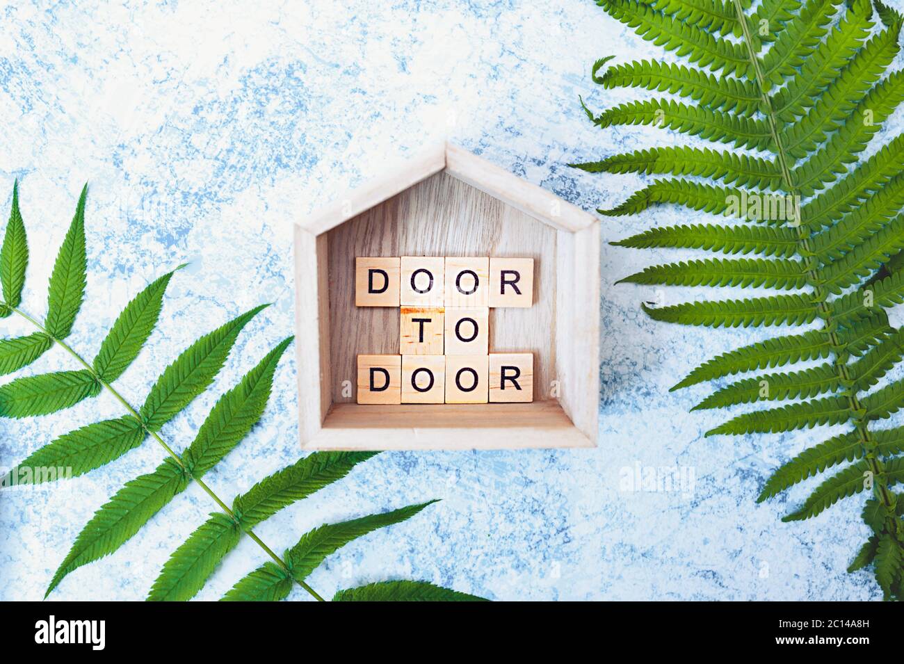 iscrizione porta a porta di lettere in legno in legno decorazione piccola casa con su un fondo grigio-blu cemento con fresche foglie verdi luminose. contactle Foto Stock