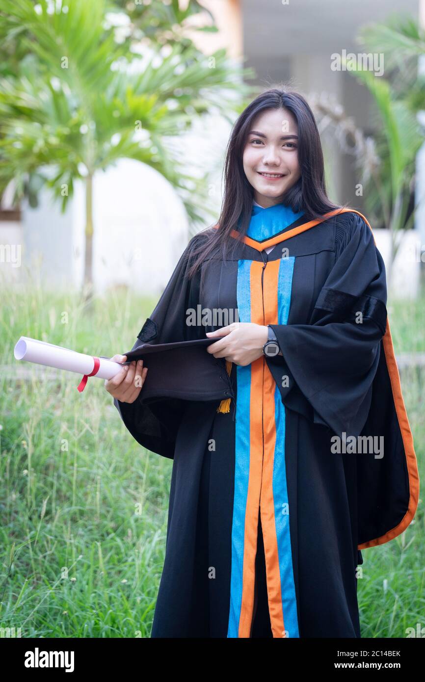 Ritratto di felice ed eccitato di giovane università asiatica laureata indossa abito di laurea e cappello festeggia con la laurea nel campus universitario Foto Stock