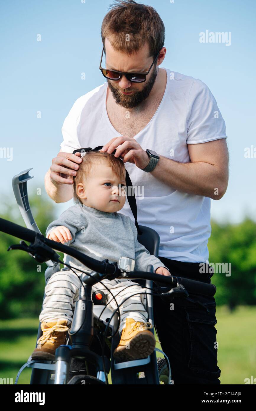 Il padre attento stringe con cura il suo bambino alla seggiolone del bambino della bici Foto Stock