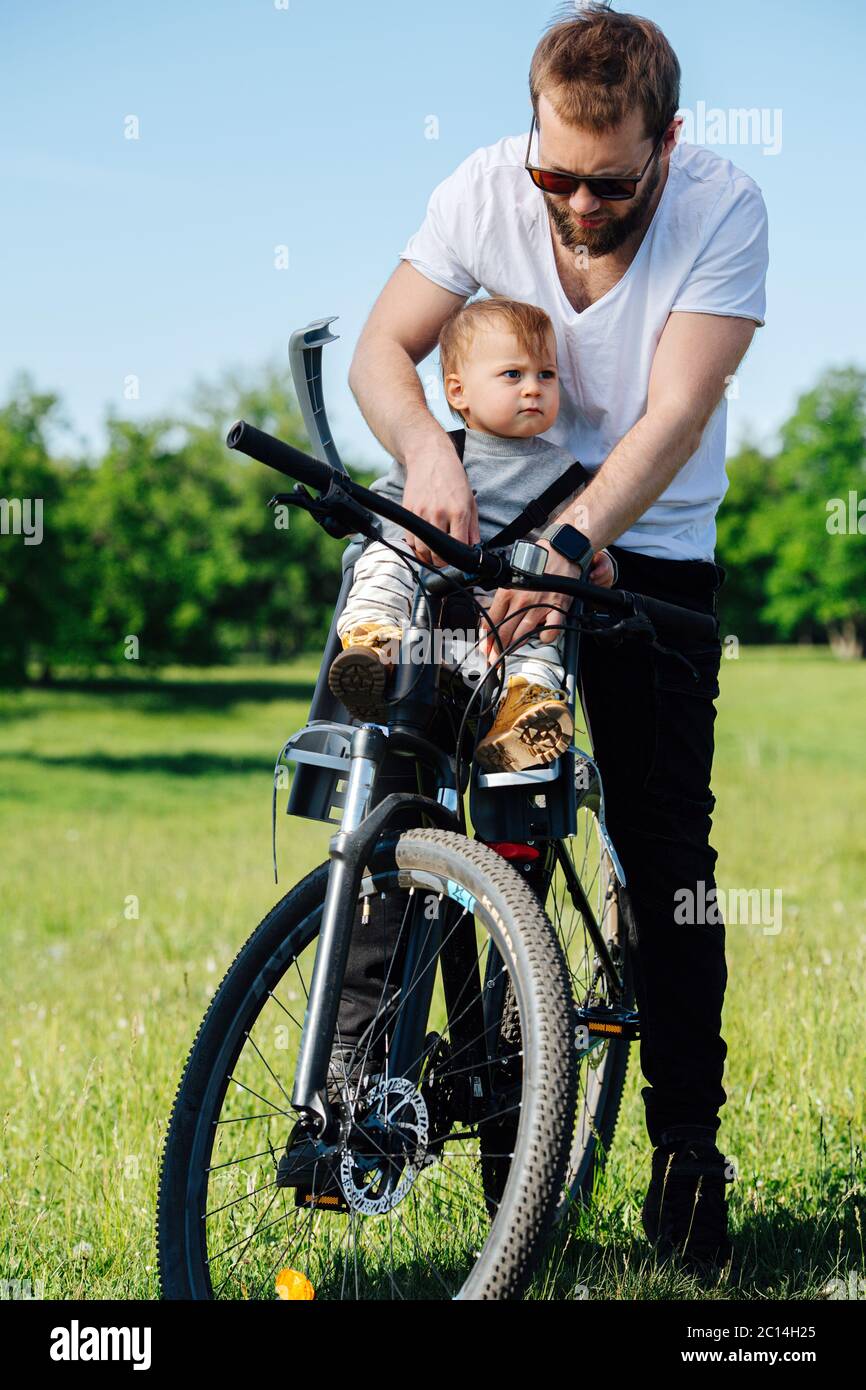 Giovane uomo sopportato desideroso di reggicaldare il suo bambino alla seggiolone del bambino della bici Foto Stock