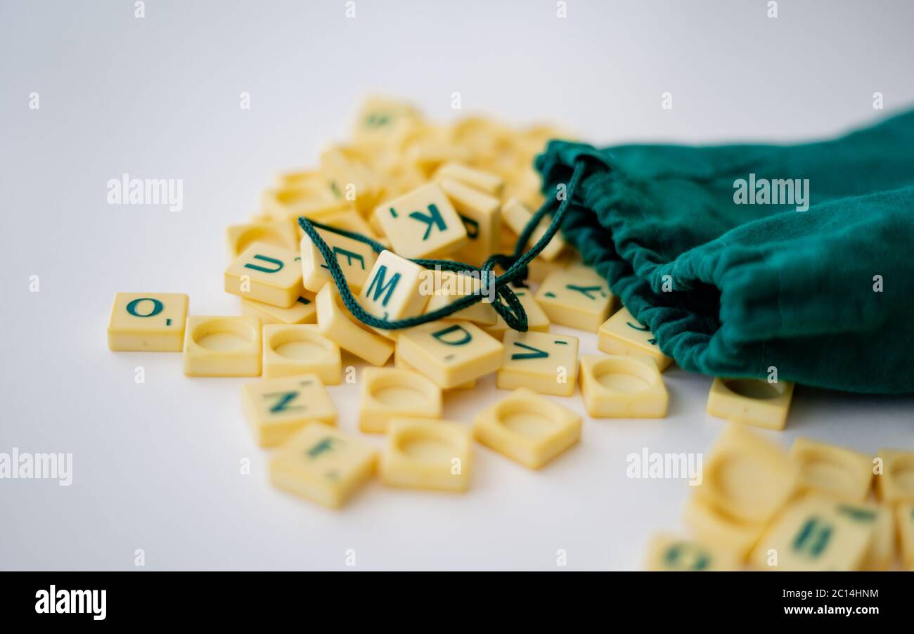 Piastrelle di lettera di gioco di Scrabble casuali con valore di punteggio che esce dalla loro borsa verde di stringa di disegno. Quarantena home entertainmentin per Coronavirus indossare Foto Stock