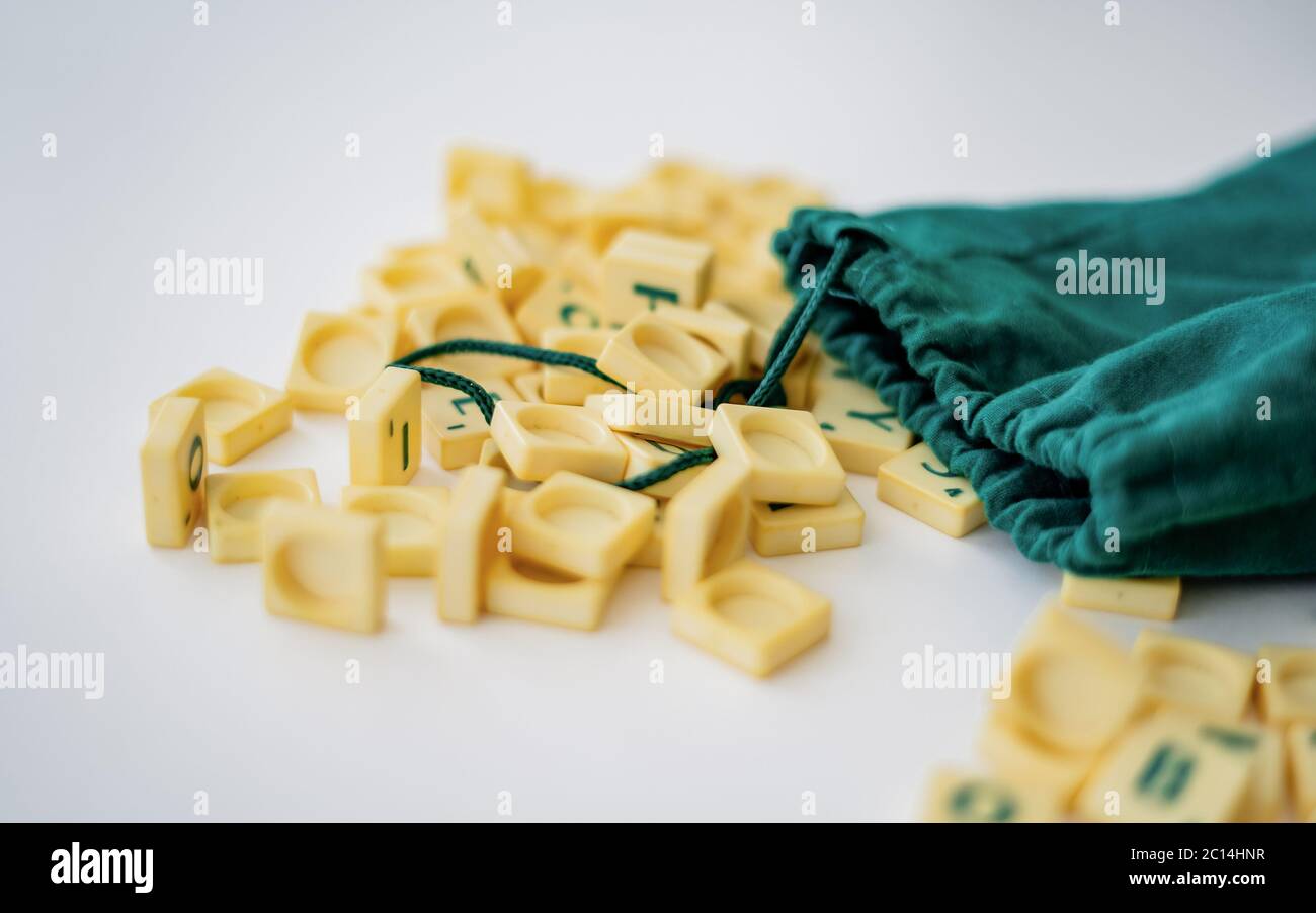 Piastrelle di lettera di gioco di Scrabble casuali con valore di punteggio che esce dalla loro borsa verde di stringa di disegno. Quarantena home entertainmentin per Coronavirus indossare Foto Stock