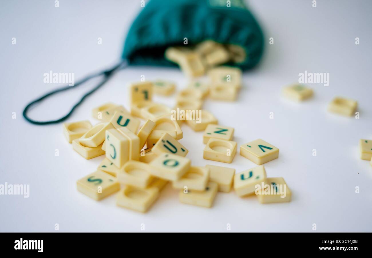 Piastrelle di lettera di gioco di Scrabble casuali con valore di punteggio che esce dalla loro borsa verde di stringa di disegno. Quarantena home entertainmentin per Coronavirus indossare Foto Stock