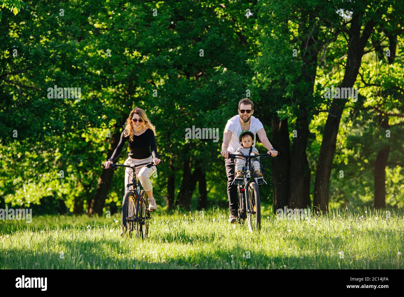 Mamma, papà e il loro figlio jolly in bicicletta sull'erba attraverso l'apertura del legno Foto Stock