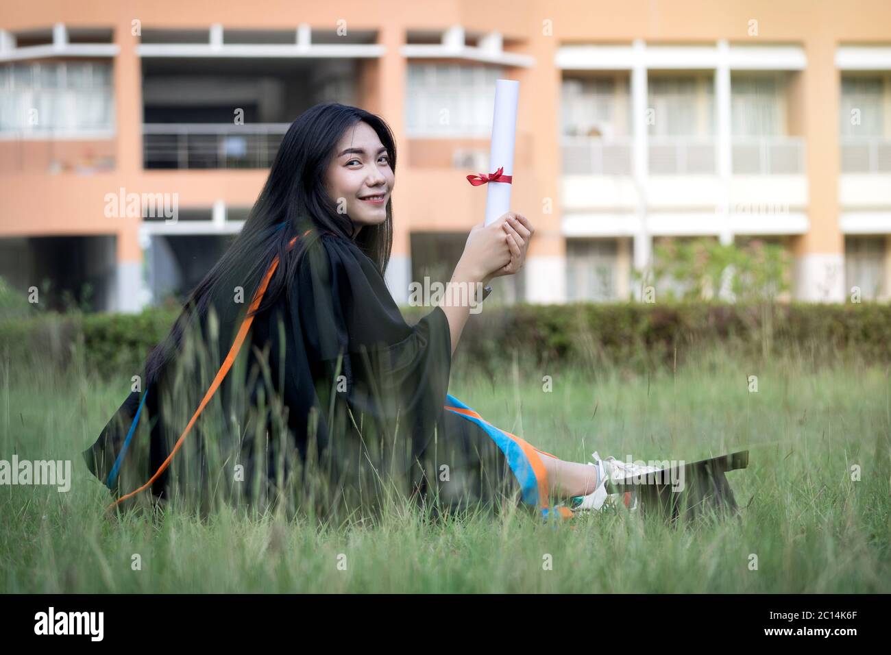 Ritratto di felice ed eccitato di giovane università asiatica laureata indossa abito di laurea e cappello festeggia con la laurea nel campus universitario Foto Stock