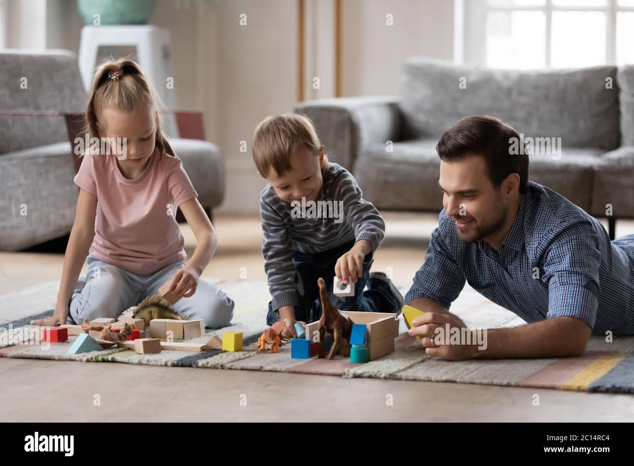 Padre con adorabili bambini che giocano con giocattoli sul pavimento caldo Foto Stock