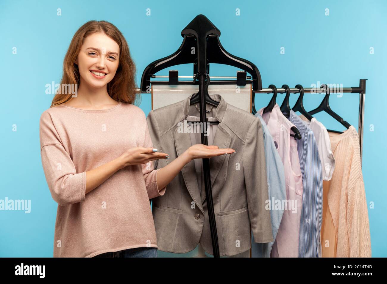 Donna felice, stilista di moda in piedi vicino vestiti appendere sullo scaffale nel negozio di stilisti, indicando la giacca classica, raccomandando stile di affari, vendendo c Foto Stock