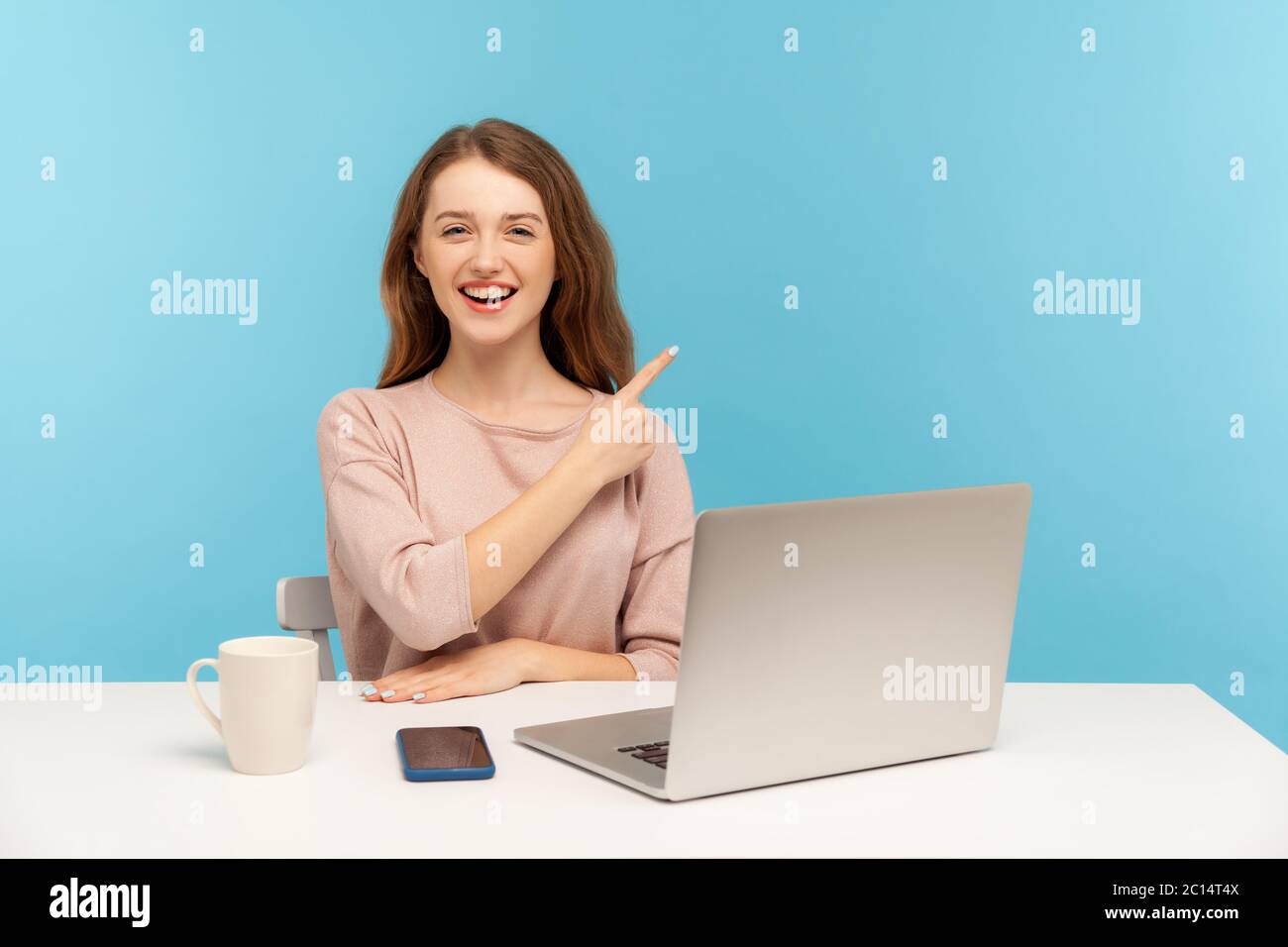 Guarda la pubblicità! Giovane donna allegra seduto in ufficio con laptop e puntando da parte, mostrando spazio per la copia di testo promozionale, comme Foto Stock