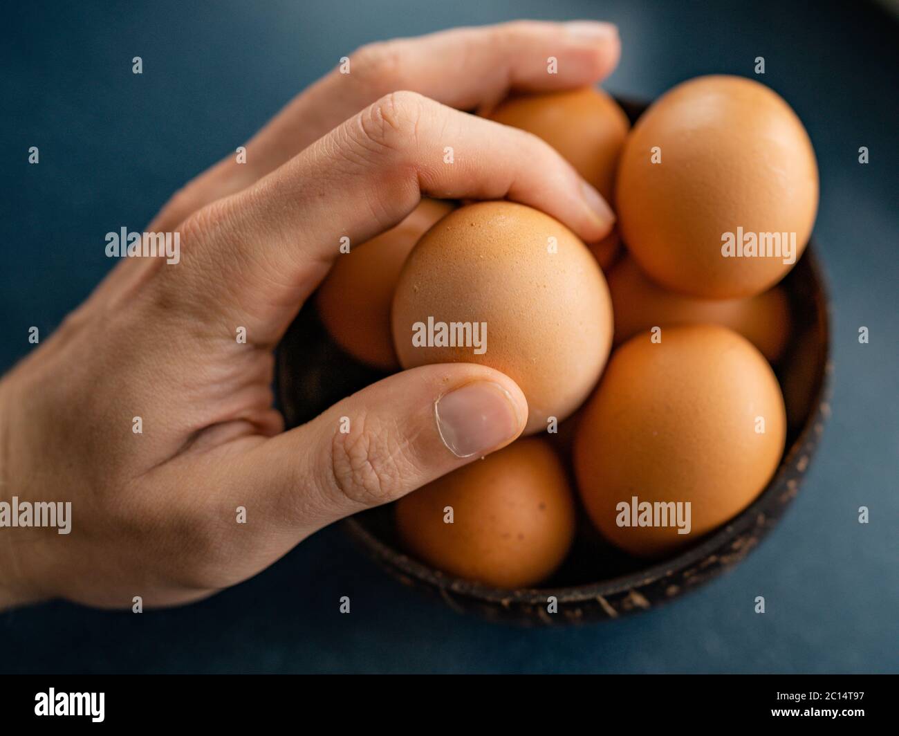 Persona che sceglie l'uovo migliore dal recipiente delle uova grezze di pollo sullo sfondo di legno. Spazio per il testo Foto Stock