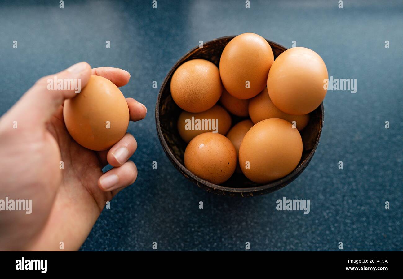 Persona che sceglie l'uovo migliore dal recipiente delle uova grezze di pollo sullo sfondo di legno. Spazio per il testo Foto Stock