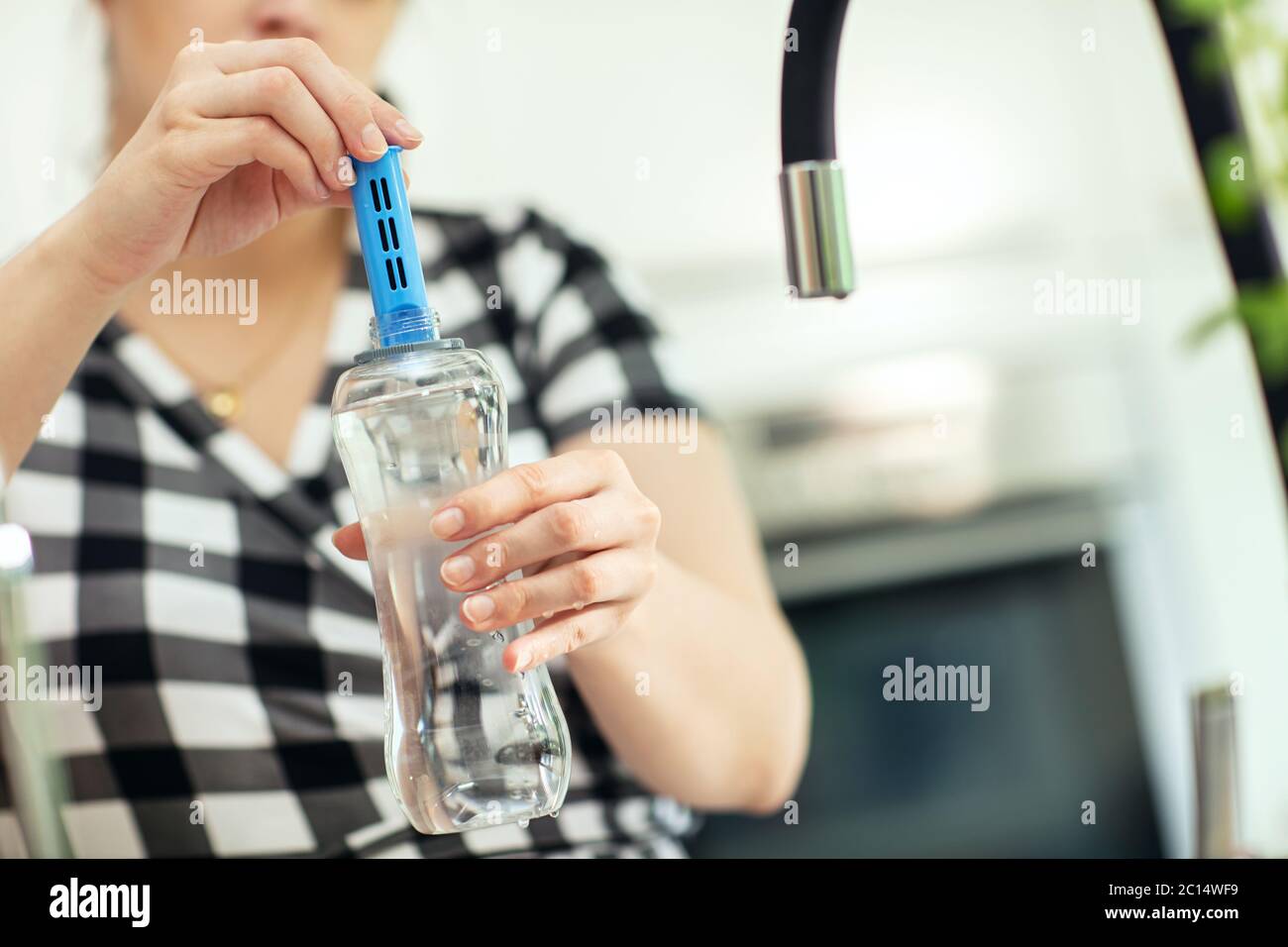 Inserimento del filtro al carbonio nella bottiglia. Donna inserisce il filtro al carbonio nella bottiglia riutilizzabile con acqua fresca in cucina. Vista frontale. Foto Stock