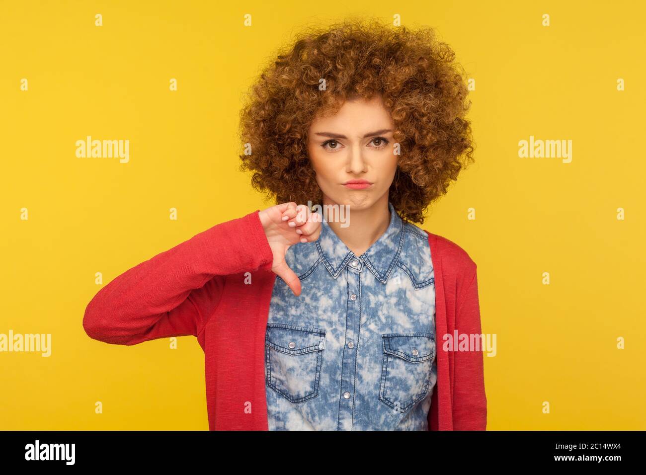 Non mi piace! Ritratto di donna sconvolto con capelli ricci in abito casual in piedi con pollici verso il basso gesto, esprimendo disapprovazione, criticando cattivo Foto Stock