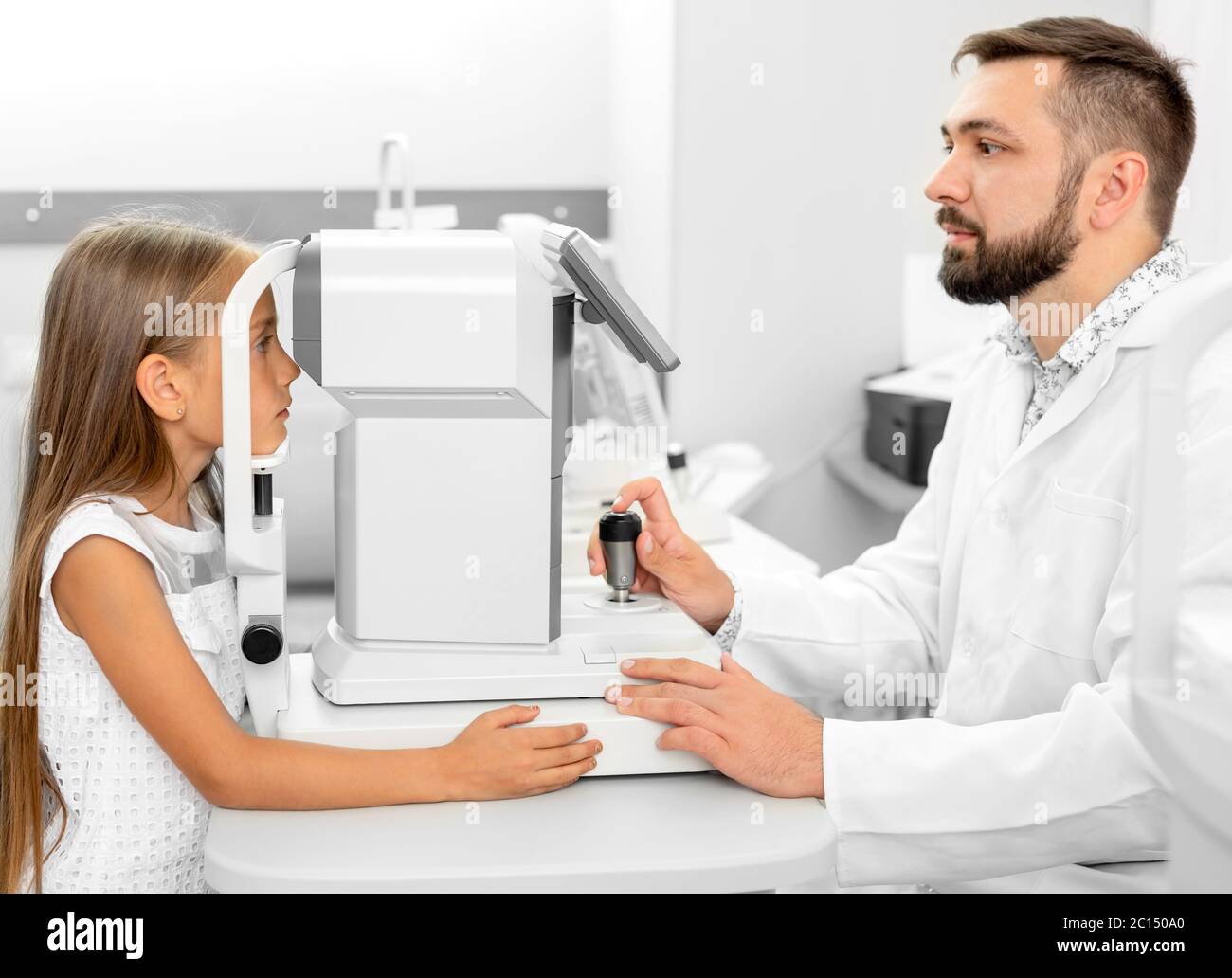 oftalmologo che tiene l'attrezzatura dell'occhio che esamina gli occhi della ragazza nella clinica Foto Stock