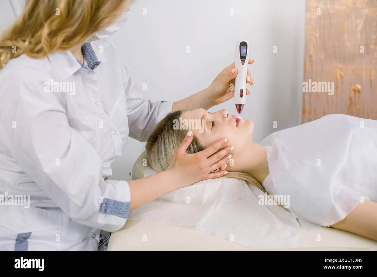 Primo piano ritratto laterale di giovane donna bionda paziente sdraiato sul divano con occhi chiusi e ottenere un trattamento laser della pelle in cosmetologia beauty spa Foto Stock