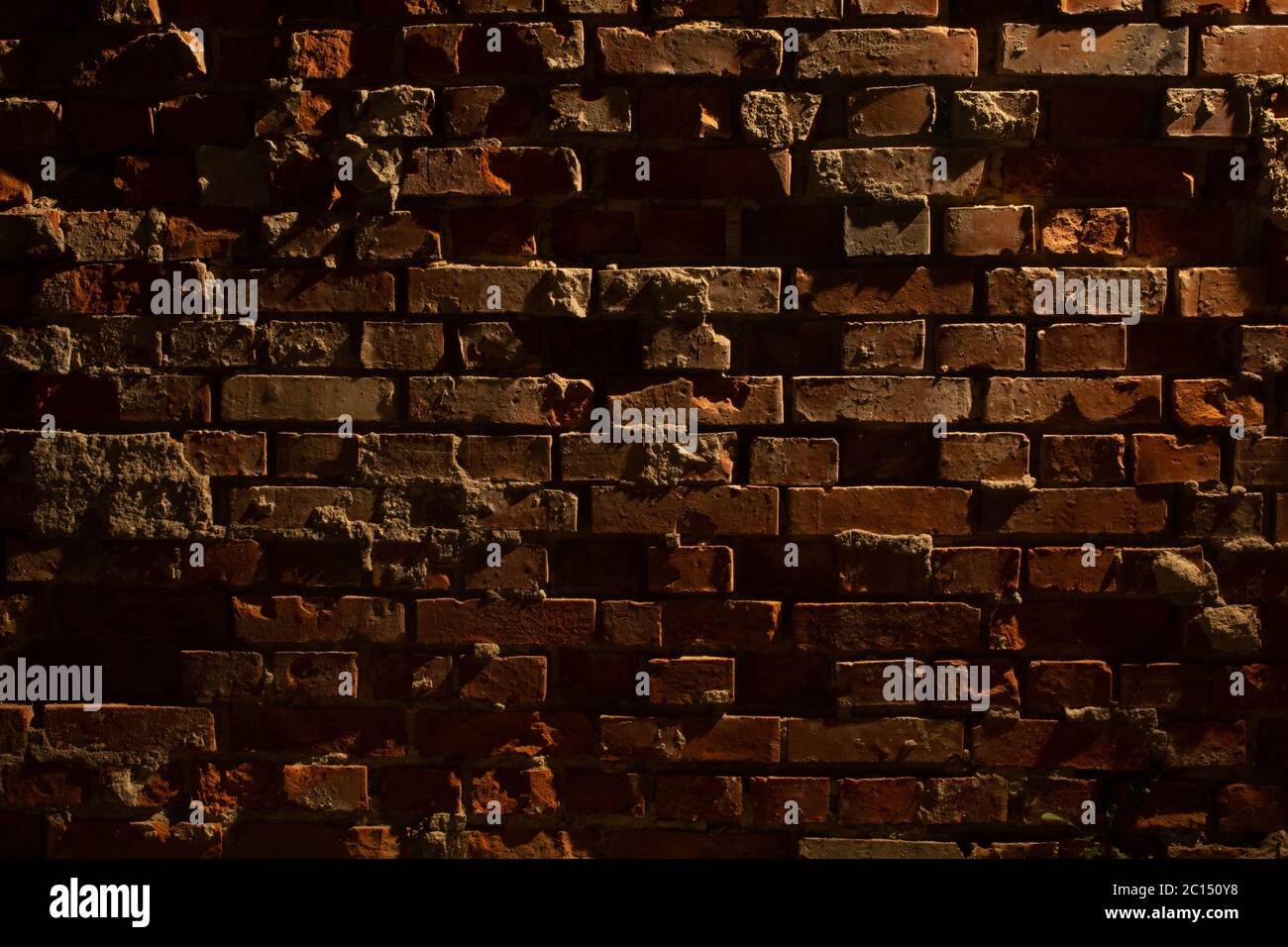 Vecchia grugia e muro di mattoni rossi danneggiato di notte con luce di una lanterna che splende su di essa Foto Stock