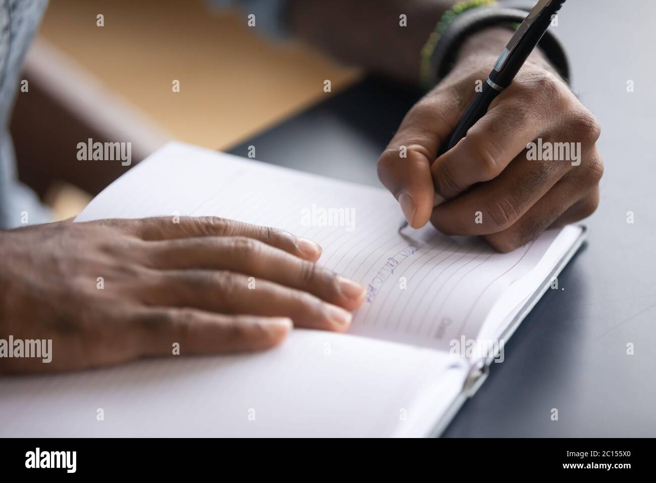 L'uomo africano seduto alla scrivania scrive informazioni sulla closeup del notebook Foto Stock L'uomo africano seduto alla scrivania scrive informazioni sulla closeup del notebook Foto Stock