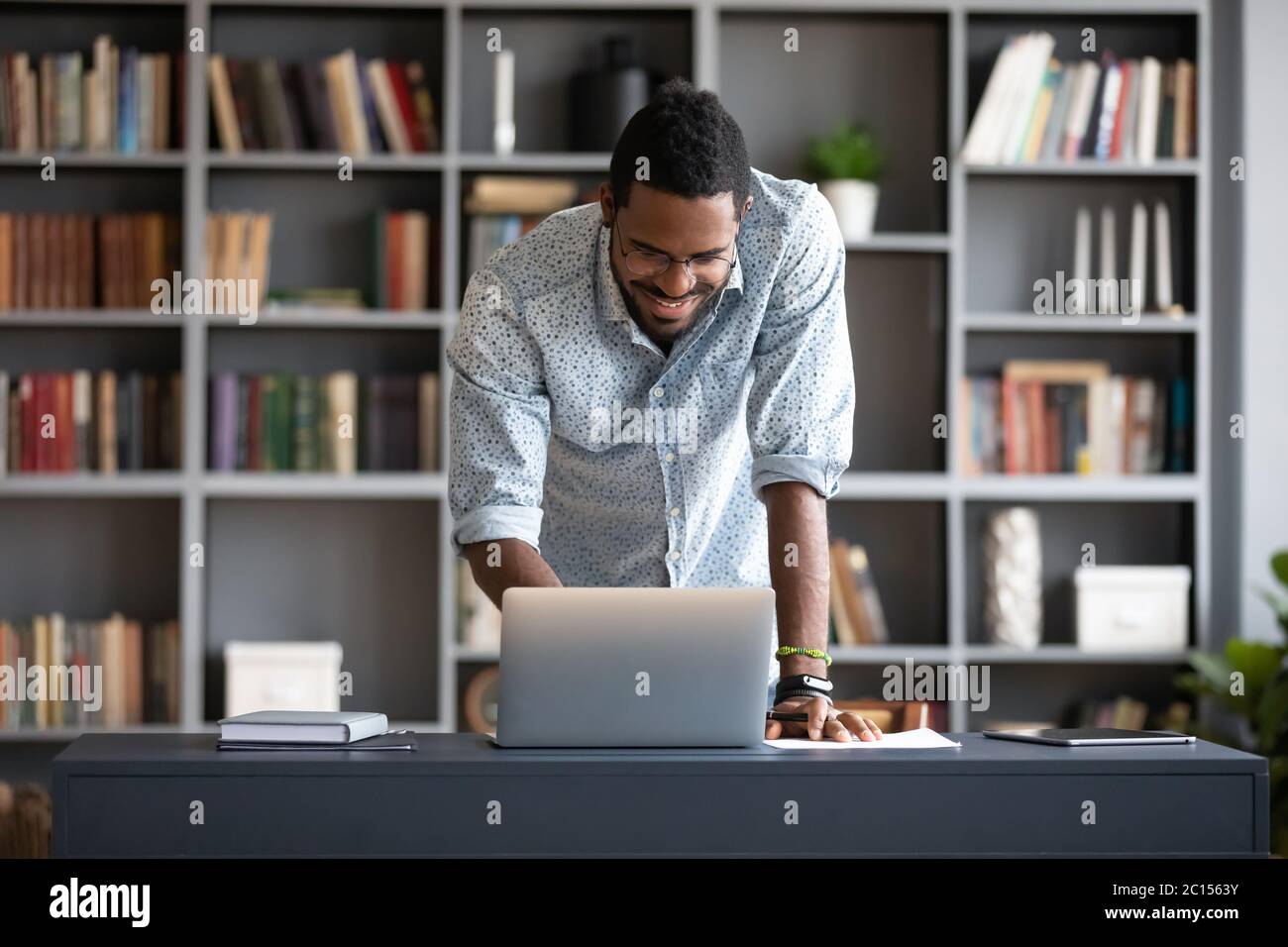 Uomo africano in piedi appoggiato su notebook godendo di una chat di comunicazione distante Foto Stock