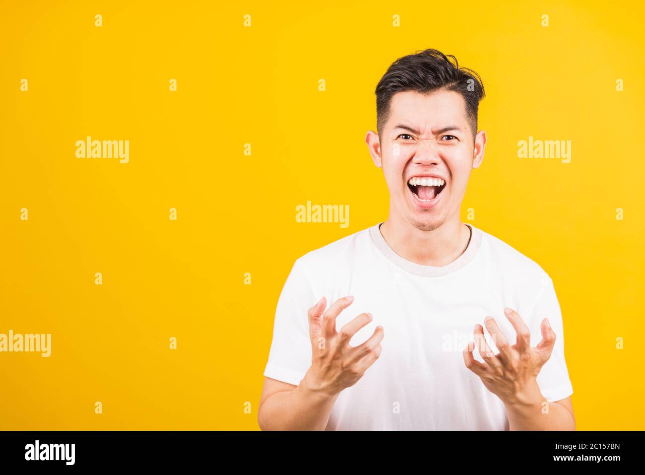 Ritratto Aaian bel giovane uomo in piedi indossando la t-shirt bianca che espressioni irate, faccia arrabbiata urlante, studio girato isolato sfondo giallo Foto Stock