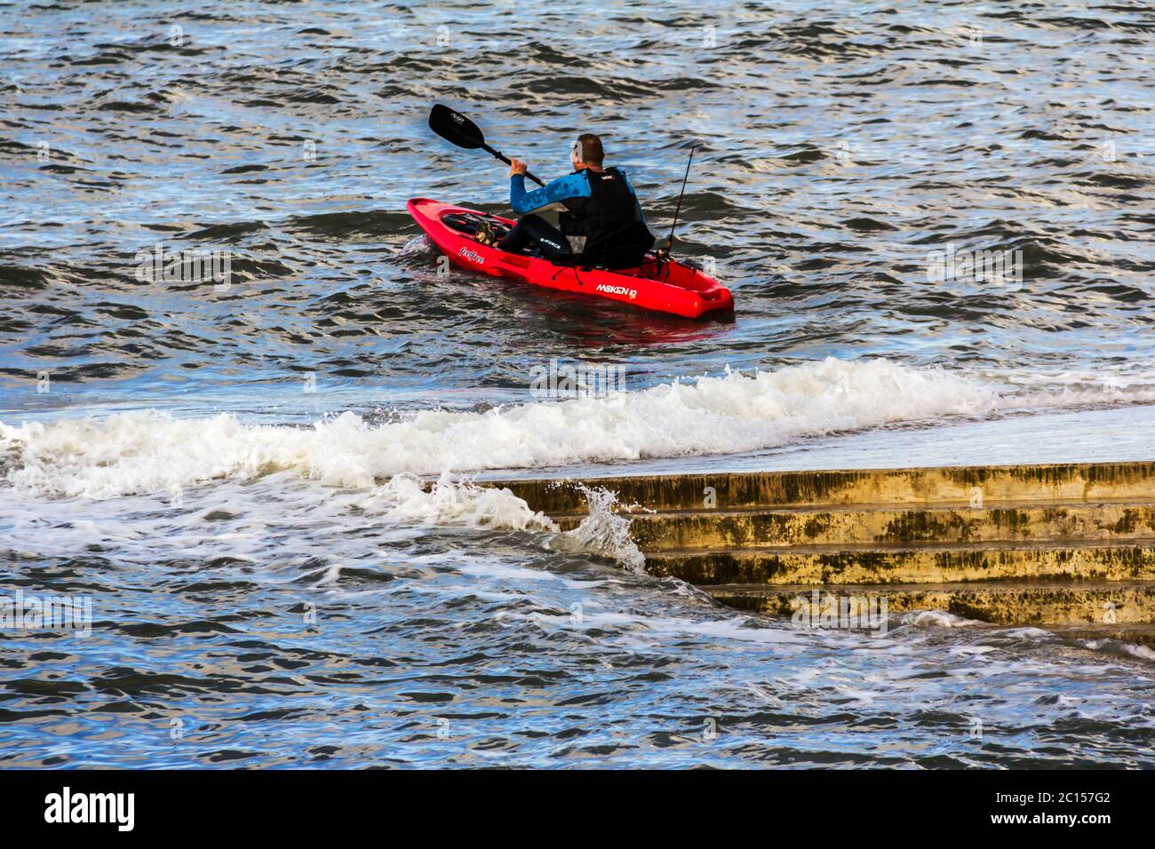 Giovane in una piccola canoa rossa sulla costa di Llanfairfechan, Galles del nord Foto Stock