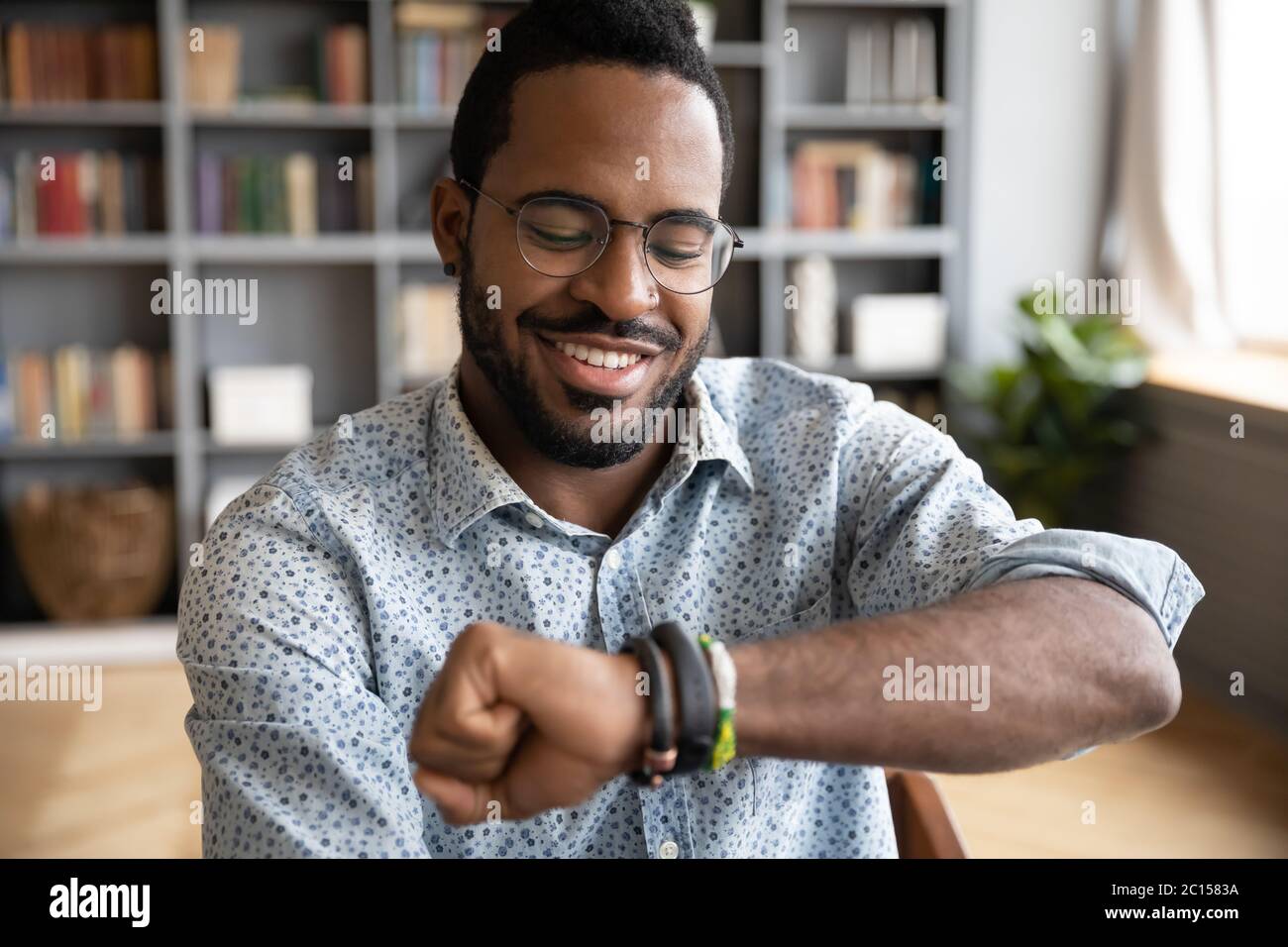 Uomo africano soddisfatto che guarda lo smartwatch goditi il nuovo dispositivo moderno Foto Stock