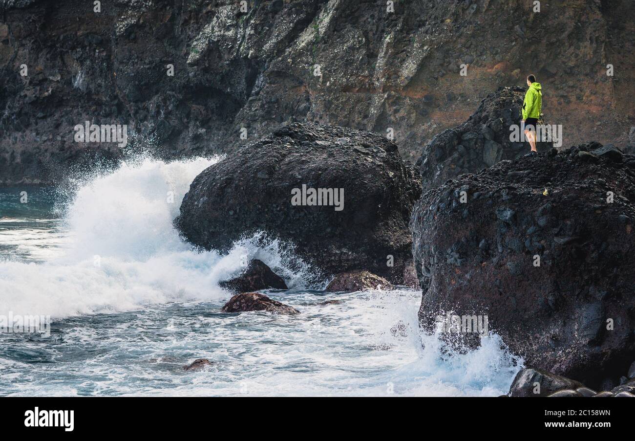 L'uomo avventuroso che si erge sulla cima della pietra sta guardando le onde grandi. Super pazzo onde in Portogallo. Foto Stock