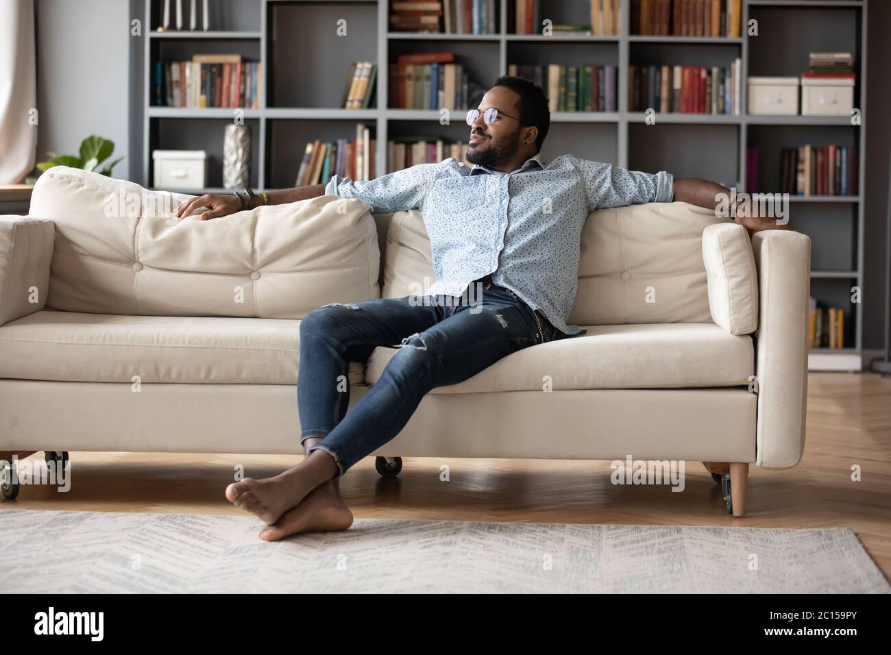 Uomo africano spensierato che riposa sul divano in un accogliente soggiorno Foto Stock