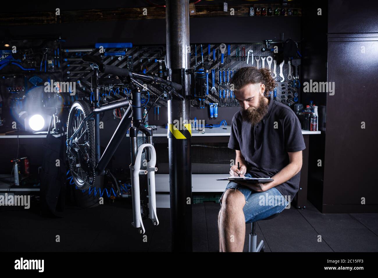 Uomo alla moda con barba, meccanico del ciclo prende appunti, lista di  controllo prima di riparare e riparare la bicicletta in officina di negozio  di biciclette. Attenzione Foto stock - Alamy