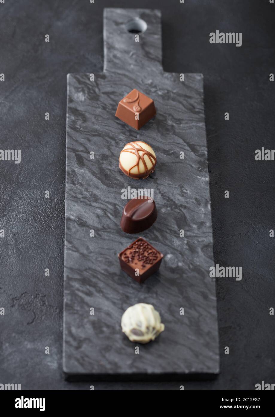 Il lusso di cioccolatini selezione sul pavimento di marmo nero a bordo. Bianco, cioccolato fondente e al latte assortimento. Vista superiore Foto Stock