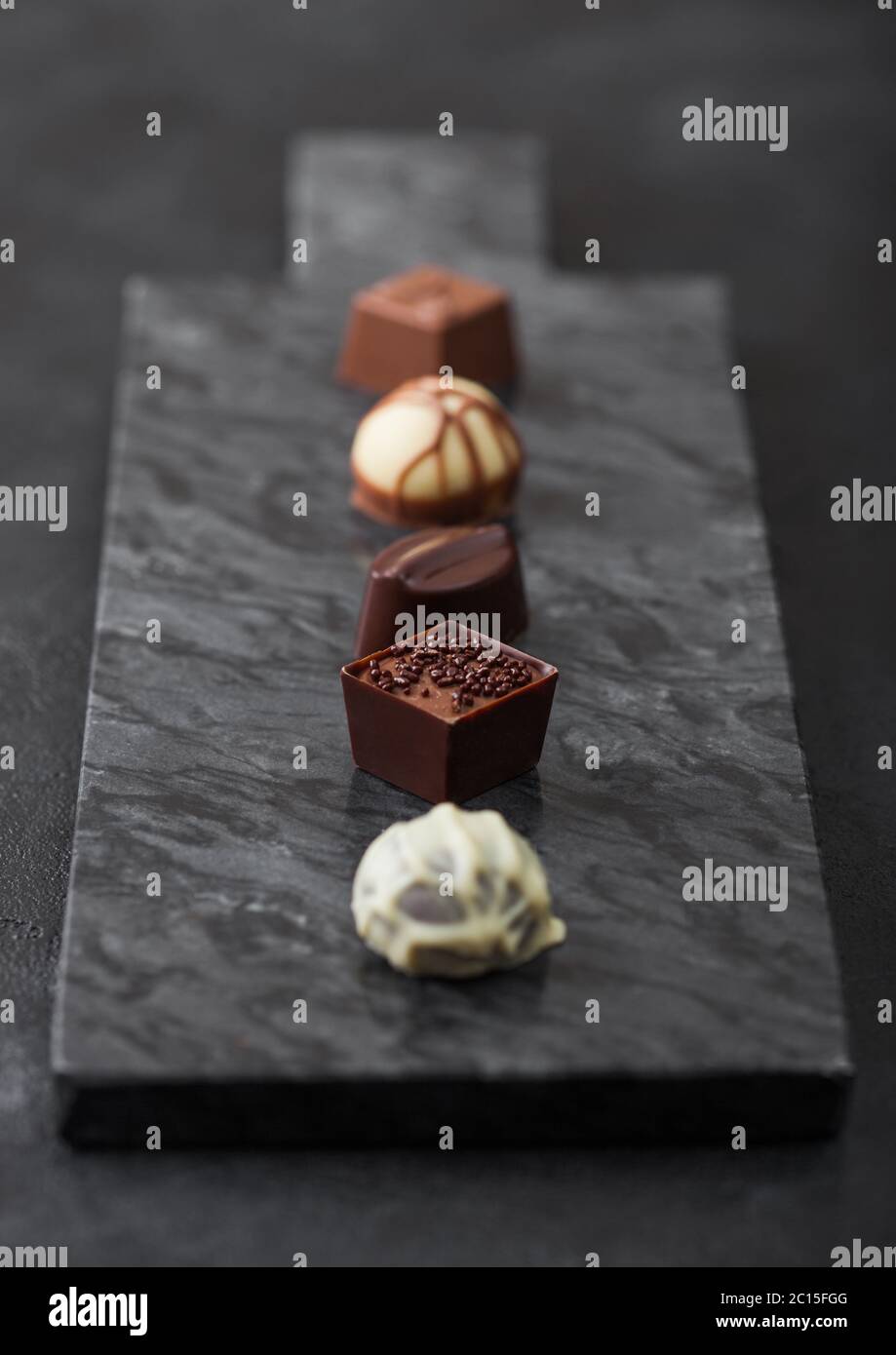 Il lusso di cioccolatini selezione sul pavimento di marmo nero a bordo. Bianco, cioccolato fondente e al latte assortimento. Vista superiore Foto Stock