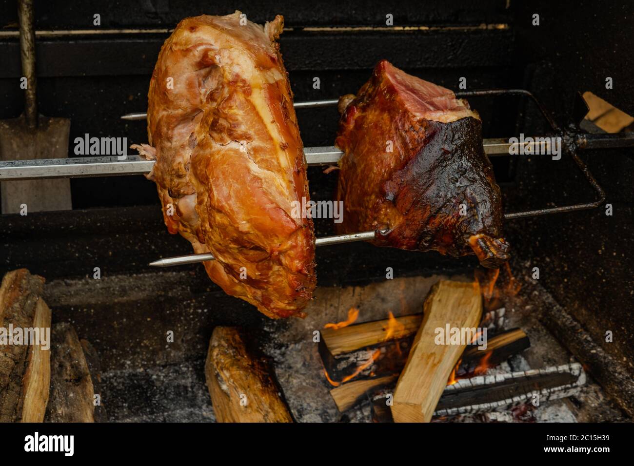 Primo piano di cottura di grandi pezzi di carne su uno spiedo di un barbecue di strada. Il prosciutto di maiale alla griglia sul fuoco aperto è un famoso piatto tradizionale della cucina ceca Foto Stock