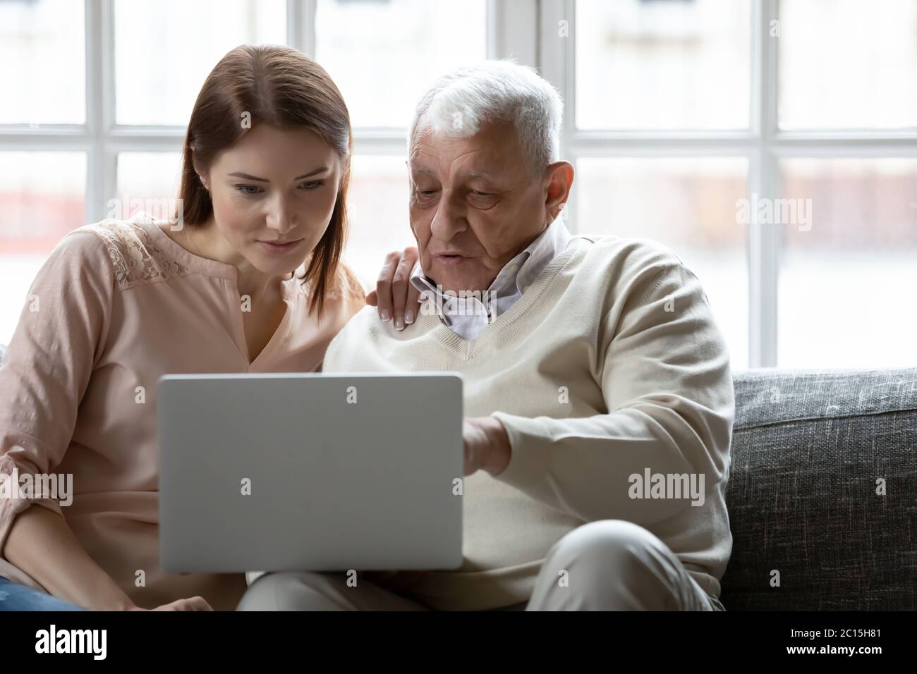 Giovane donna e uomo anziano che usano il laptop insieme a casa Foto Stock